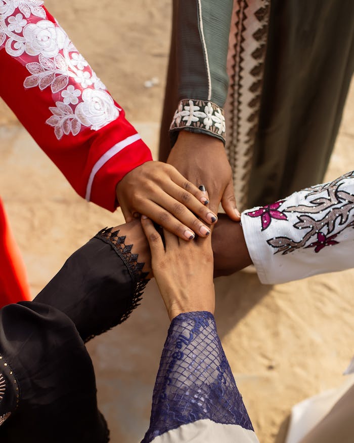 A group of people joining hands wearing colorful traditional attire outdoors, symbolizing unity.
